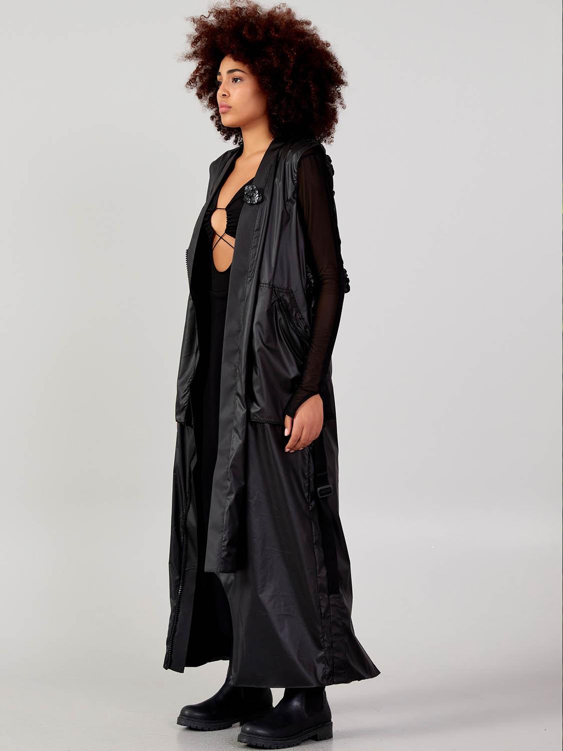 Side view of a women’s black long cardigan vest with adjustable straps and flowing asymmetric length at VVC SHOP Sitia