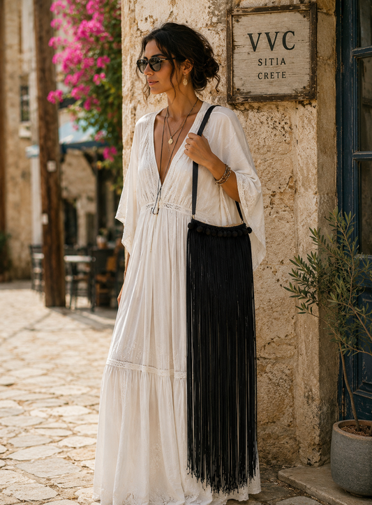 Woman in a white and black dress standing in front of a stone building with 'VVC SITIA CRETE' sign.