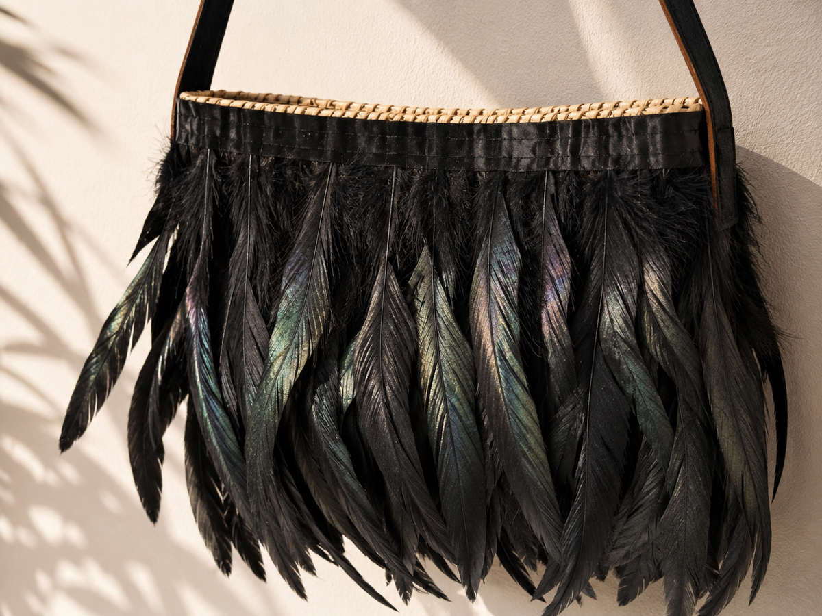 Close-up detail of a handmade raffia bag decorated with black iridescent feathers, highlighting artisanal craftsmanship and natural materials.