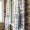 Checkered curtain with tassel tieback against a stone wall