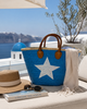 VVC turquoise beach basket with white star design styled with a blonde woman in white linen fashion on a Greek island holiday in Santorini.
