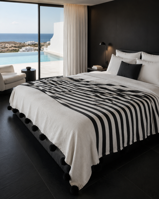 Folded VVC organic cotton striped blanket in black and off-white, handmade in Morocco with soft woven texture and black wool pompoms for bedroom styling