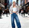 Woman in a fur coat and jeans standing on a busy city street.