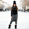 Woman wearing a black coat, gray scarf, black beanie, and gray harem pants on a city street.