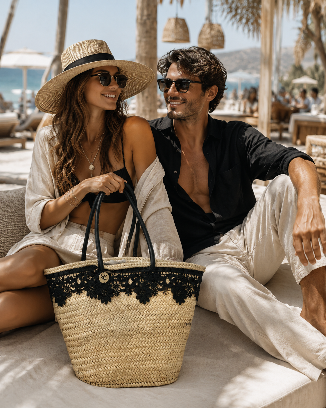 Luxury raffia designer tote bag with black lace detail and round handles in Sitia Crete Couple sitting together with a straw bag featuring black lace details, beach setting.