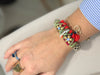 Close-up of a wrist wearing the ART WEAR Dimitriadis bracelet with bronze-tone flowers, strass and red pom-poms.