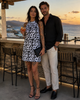 bikini BEACHWEAR black and white animal print halter mini dress styled at a golden-hour cocktail bar in Mochlos, Crete, worn with black high-heel sandals and a black clutch beside a male model with sea view in the background.
