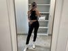 Woman wearing a black bandeau top with black laminated slim-fit viscose-blend pants in a Mediterranean courtyard.