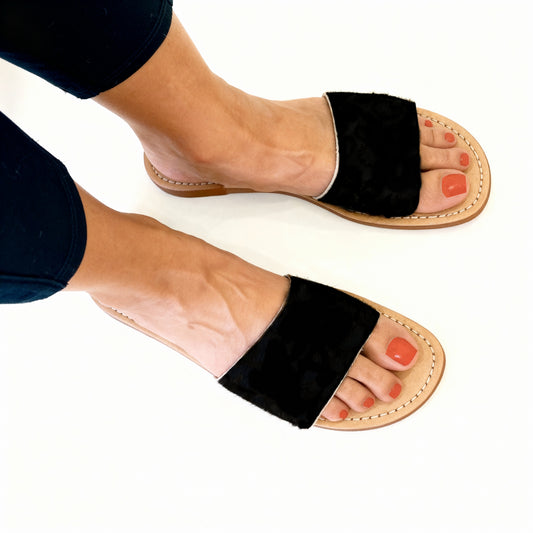 Black leather fur sandal open-toe sandals worn on feet with a white background handmade vvc shop sitia crete summer essential slipon sandal comfortable shoe