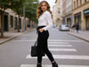 Side view of a woman walking in black slim-fit fine-knit wool jogger trousers while carrying a black jacket.