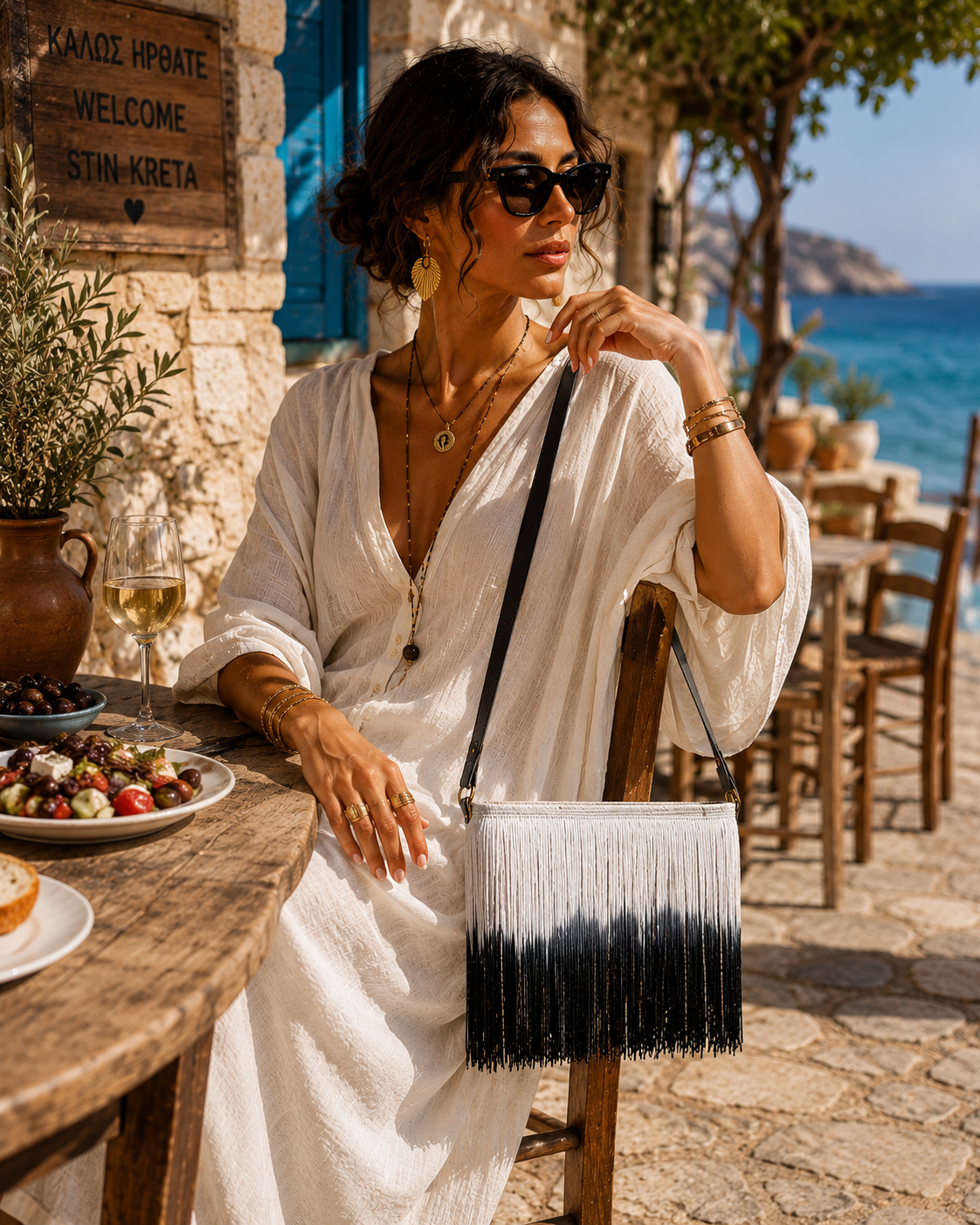 Boho raffia fringe shoulder bag in black and white ombré by VVC, worn with a white summer dress in Sitia Crete