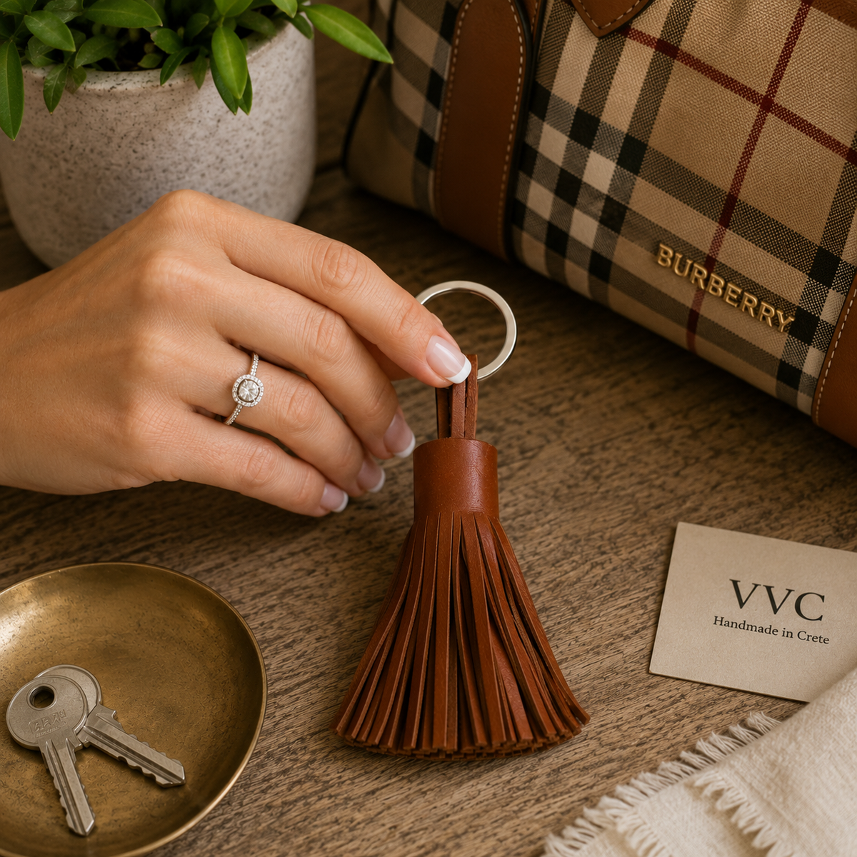 Woman with French manicure and diamond ring holding a handmade camel brown leather tassel key chain by VVC™, crafted in Crete from genuine leather and styled with luxury handbag accessories.
