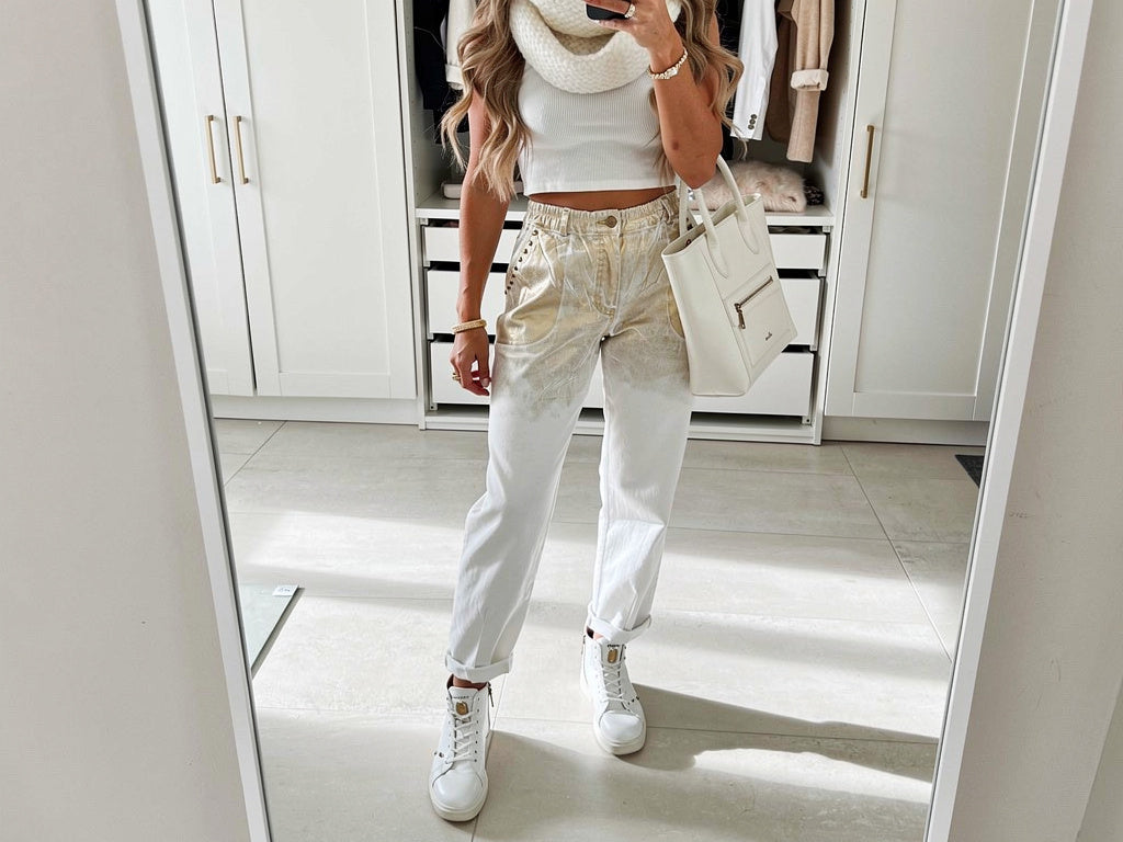 Front view of gold and white laminated shimmer trousers with relaxed tapered fit, rolled ankle cuffs and adjustable waist belt