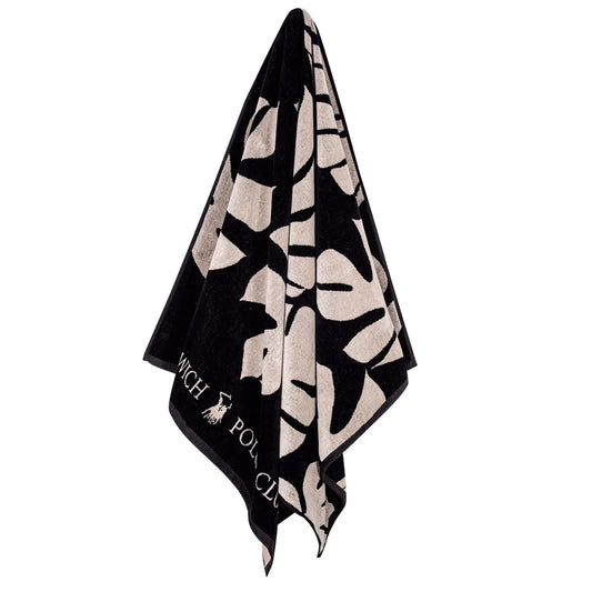 Hanging Greenwich Polo Club 3773 black and beige tropical leaf cotton beach towel with fringed ends.