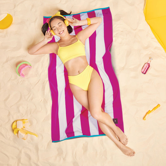 Woman relaxing on a Greenwich Polo Club 3817 fuchsia and white striped beach towel on sand.