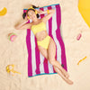 Woman relaxing on a Greenwich Polo Club 3817 fuchsia and white striped beach towel on sand.
