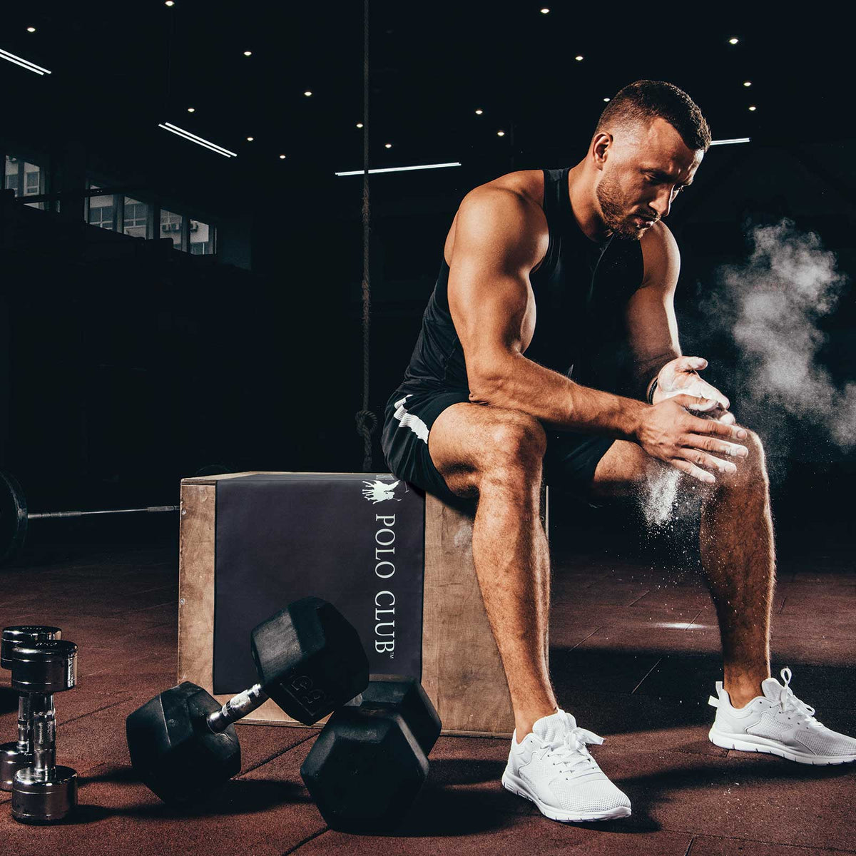 Athlete sitting on a box with dumbbells and a 'Polo Club' branded box in a gym setting. Greenwich Polo Club Gym Towel 4183 in black microfiber with roll-up loop.
