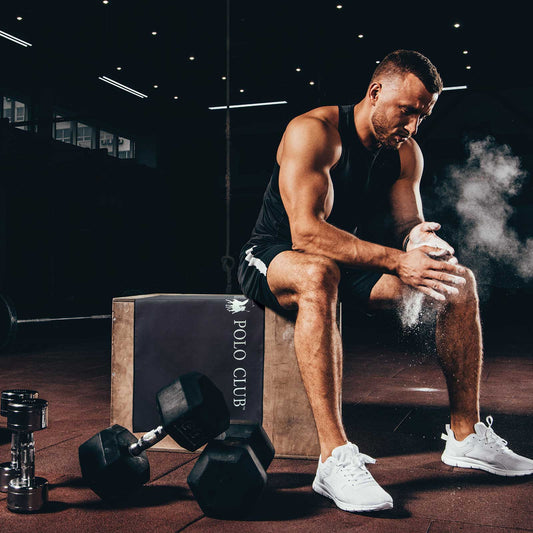 Athlete sitting on a box with dumbbells and a 'Polo Club' branded box in a gym setting. Greenwich Polo Club Gym Towel 4183 in black microfiber with roll-up loop.