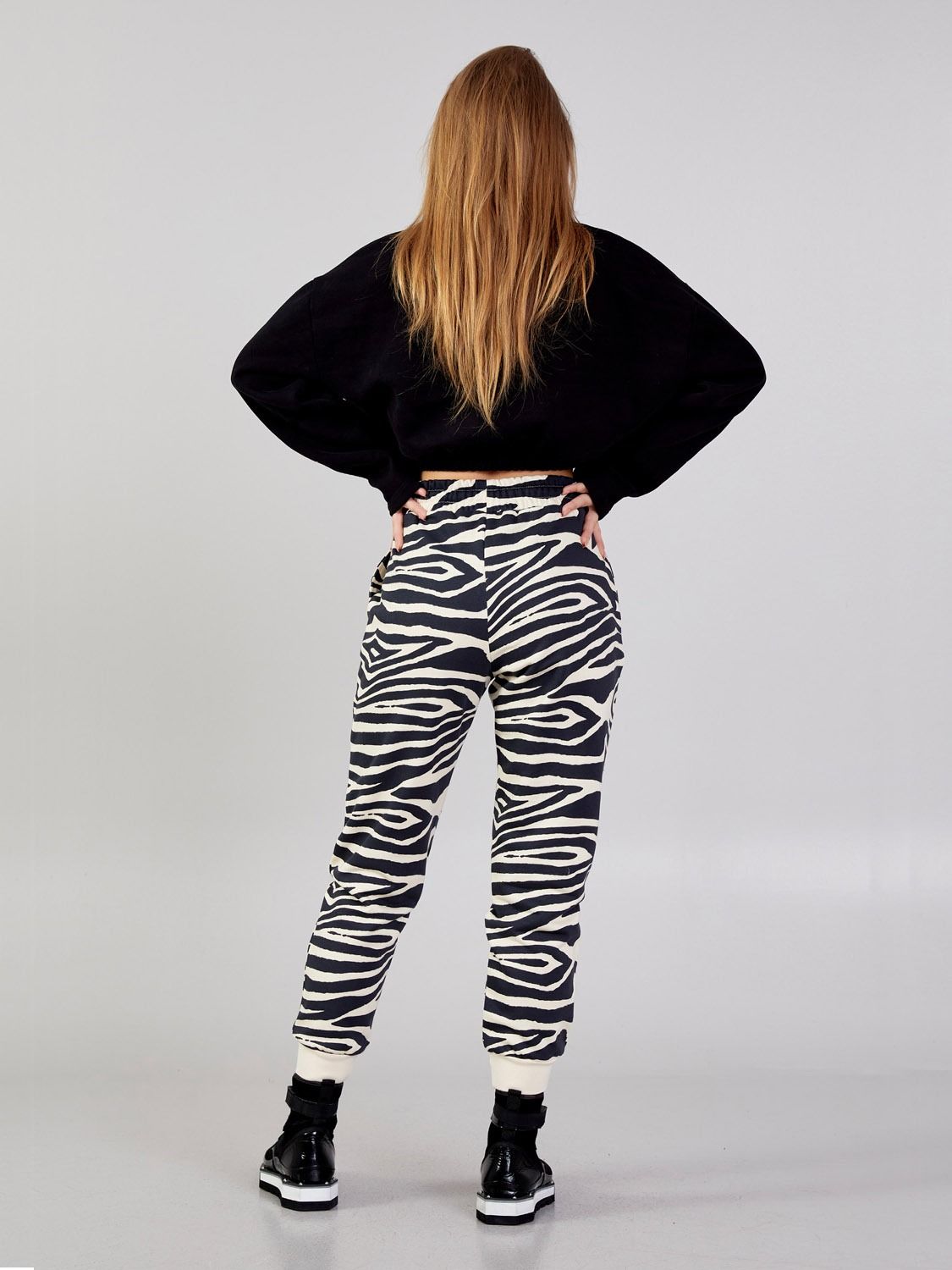 Full-length back view of a model wearing Kasha beige-and-black zebra-print cotton-blend jogger pants with a black top.