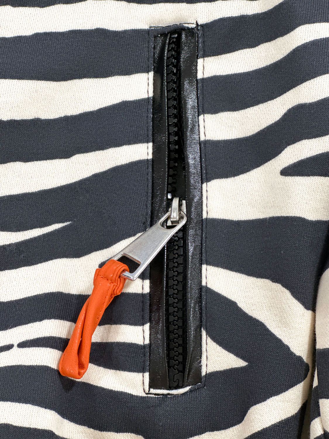 Close-up of the Kasha zebra bomber jacket zip pocket with black trim and orange pull detail
