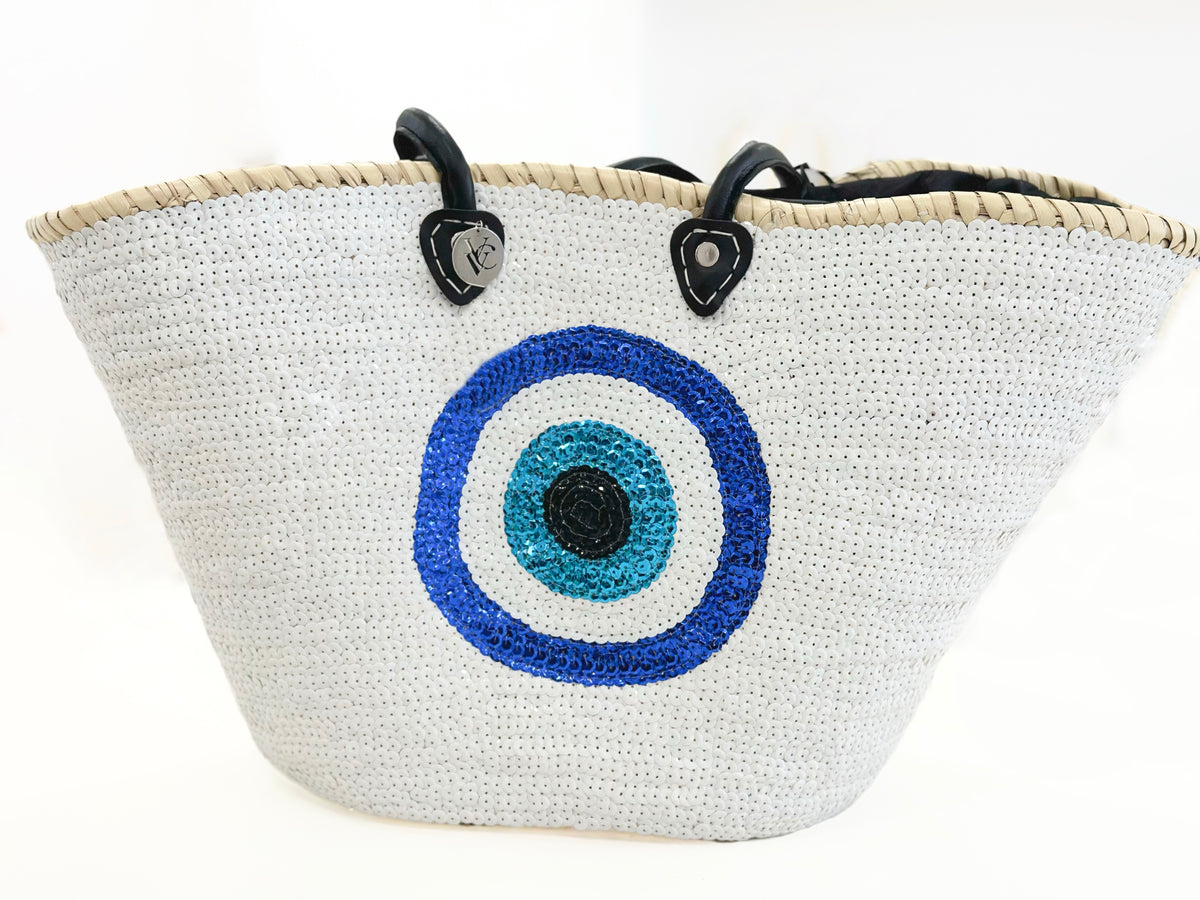Large white sequin beach basket with blue evil eye motif, black handles and natural straw trim.
