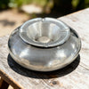 Metallic ashtray on a wooden surface with a blurred natural background