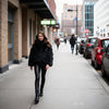 Woman in a black fur coat and leather pants walking on a city street.