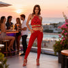 Woman wearing the Melody red macramé top with gold bone-shaped embellishments and matching red trousers in Sitia.