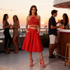 Front view of a woman wearing the Melody red macramé top with gold embellishments and a matching red maxi skirt.
