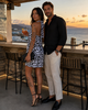 MiandMi black and white animal print viscose halter mini dress shown from the side and back at a golden-hour cocktail bar in Mochlos, Crete, styled with black heels and a quilted clutch.