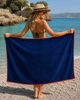 Luxury MiandMi cotton beach towel with coral print and fringed edges styled at a Greek island resort