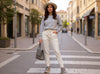 Front-side view of a woman walking in off-white slim-fit fine-knit wool jogger trousers with a grey top.