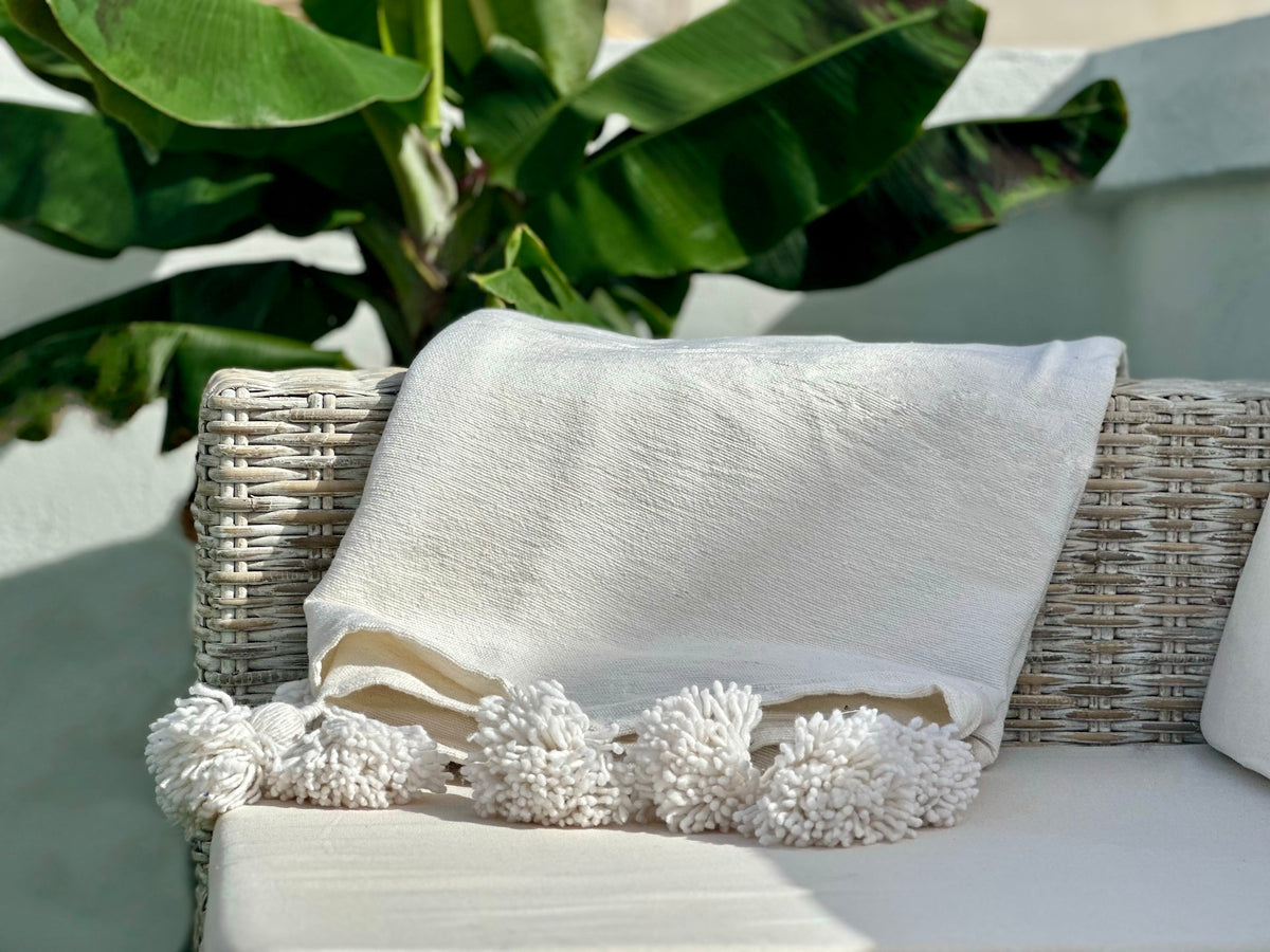 close up of white VVC cotton blankets  neatly folded and displayed on a couch,  with pom-pom detail.