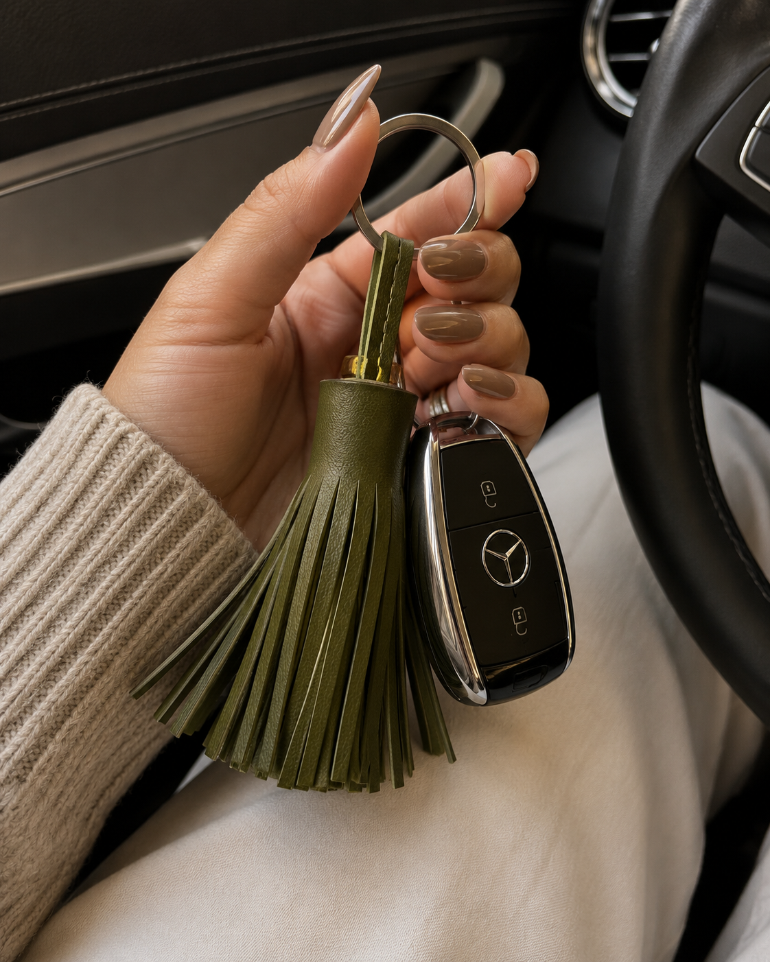Woman holding an olive green leather tassel key chain with car keys in a luxury vehicle interior, handmade leather accessory from Crete available in Sitia and online