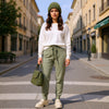 Full-length front view of a woman wearing olive-green slim-fit fine-knit wool jogger trousers on a city street.