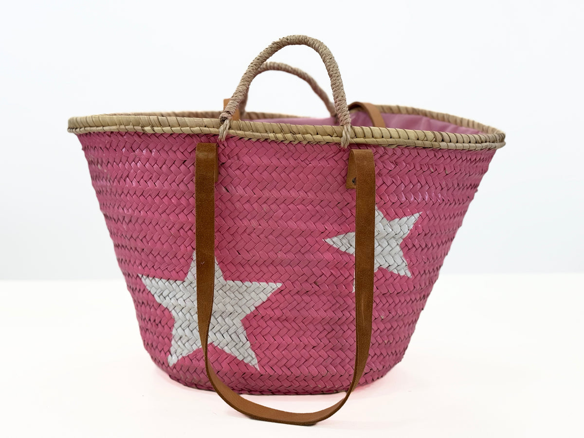 Rear view of pink woven beach basket with leather straps and pink textile inlet on white background.