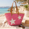 Handmade pink straw basket with white stars and long leather straps for shoulder carry.