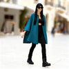 Woman wearing a teal coat, black top, and pants in an urban setting