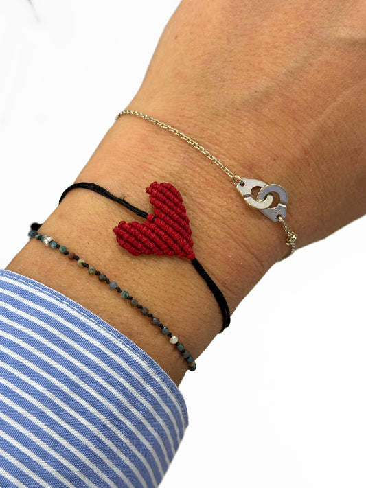 Close-up of a wrist wearing layered bracelets with a red heart charm.
