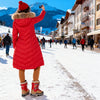 Person in a red coat taking a photo of a snowy mountain and town scene.