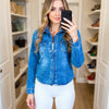 Woman taking a mirror selfie wearing a blue denim jacket and white pants in a closet.