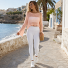 Front view of the soft peach open-knit cropped summer top styled with flowing white trousers in Sitia, Crete.
