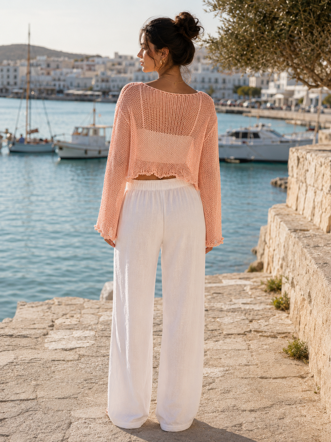 Straight back view of the soft peach open-knit cropped top worn with white trousers at VVC SHOP Sitia, Crete.