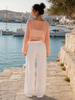 Straight back view of the soft peach open-knit cropped top worn with white trousers at VVC SHOP Sitia, Crete.