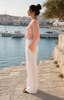 Side view of the soft peach open-knit cropped top with bell sleeves and white summer trousers in Sitia.