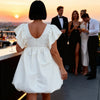 Vicbee off-white babydoll mini dress with oversized puff silhouette, styled for wedding guest looks and summer events in Crete back view