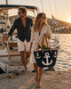 Stylish couple leaving a sailing boat in Crete carrying a handmade VVC™ anchor beach basket filled with wine and local food. Luxury beach bag, travel tote and unique gift idea from Sitia, Crete.