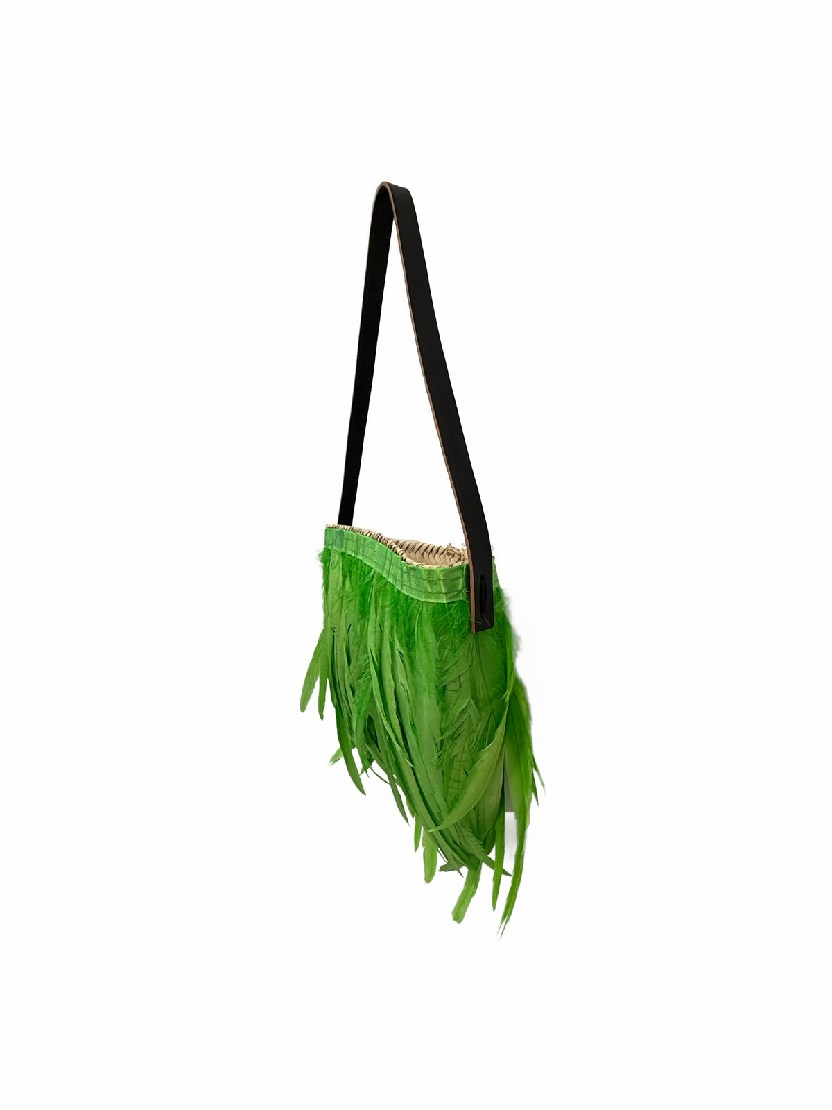 Side view of small handmade raffia shoulder bag with apple green feathers and slim black shoulder strap on white background