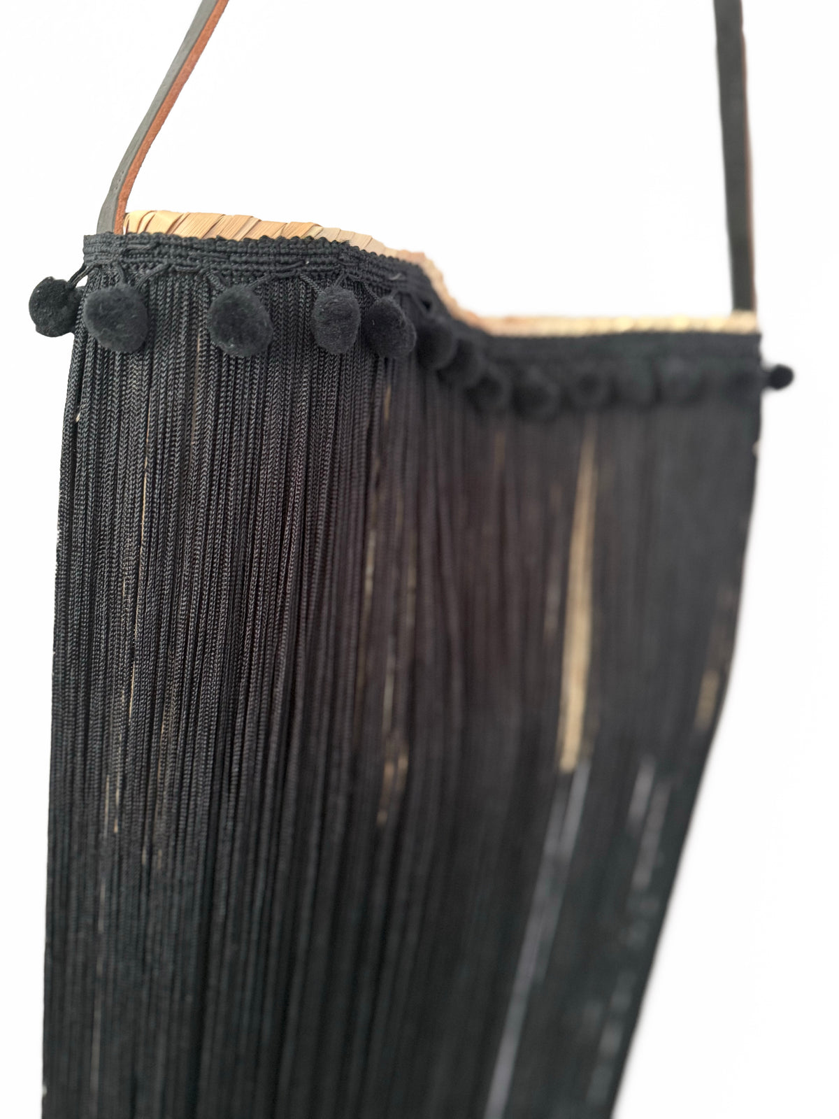 Close-up of handmade black fringe raffia shoulder bag by VVC with pompom trim, woven body and long satin fringes in Sitia Crete