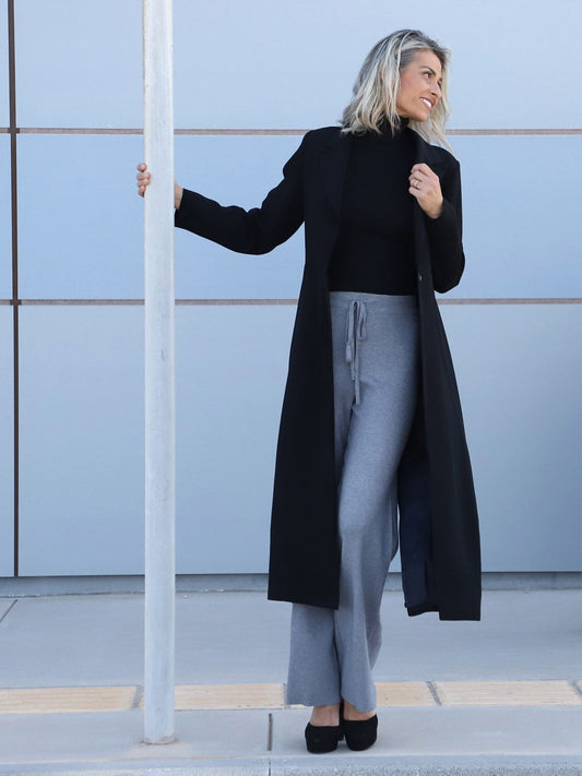 VVC™ women’s black longline blazer styled with grey wide-leg trousers, front view, made in Greece for VVC SHOP Sitia, Crete.